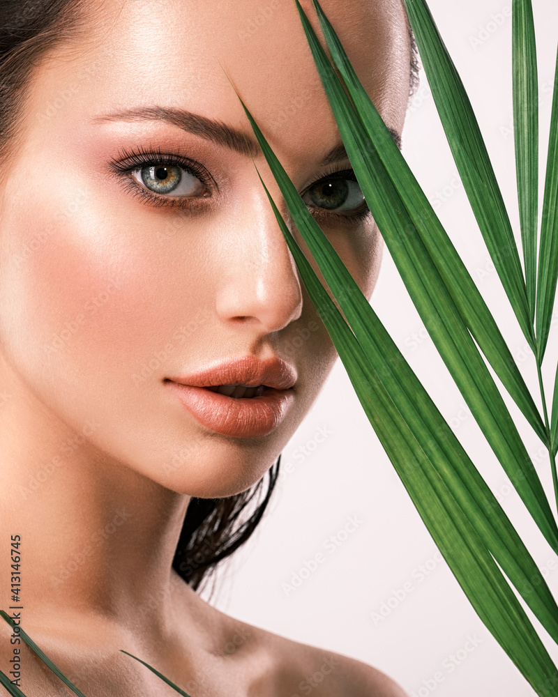 Wall mural young beautiful woman with green leaves near face. skin care beauty treatments concept. closeup girl