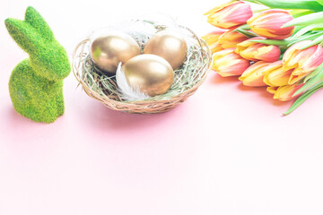 Easter eggs Golden color in basket with spring tulips, white feathers on pastel pink background in Happy Easter decoration. Festive decoration.