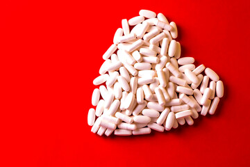white medicine pills in the shape of a heart on a red background. The pills form the heart. Healthy lifestyle concept treatment choice. Pharmaceuticals. Copy space. 
