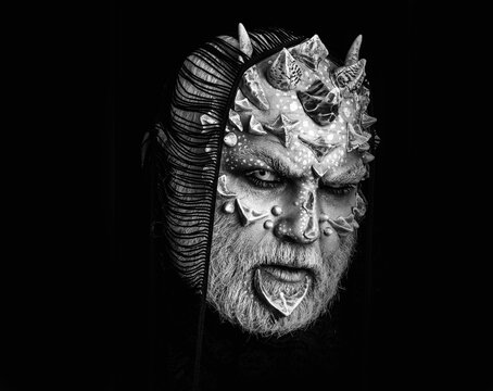 Devil man with fictional makeup. Demon with scarf on head isolated on black. Monster with white eyes and thorns on face. Alien with dragon skin and grey beard.