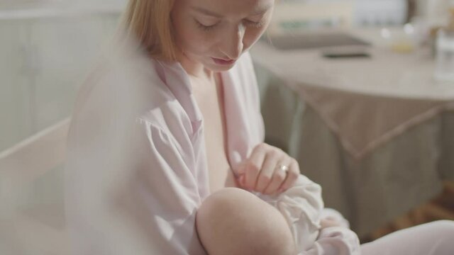 Tilt down shot of beautiful blonde mother smiling and breastfeeding baby at home