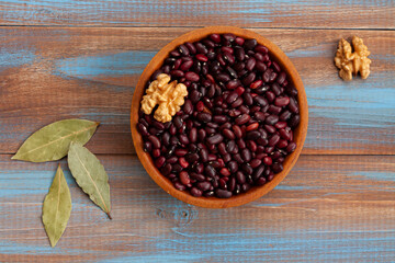 haricot beans in a wooden bowl, walnuts and laurel leaves on blue and brown wood boards