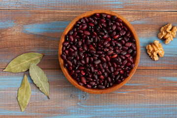 haricot beans in a wooden bowl, walnuts and laurel leaves on blue and brown wood boards