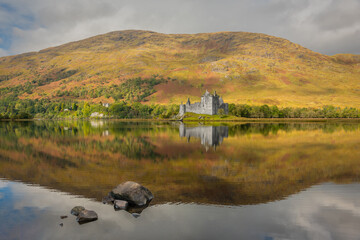 Kilchurn castle in Scotland. Looking over Loch Awe, the castle is perfectly reflected in the still water. Autumn colours in the hills behind