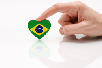 Love and respect Brazil. A man's hand holds a heart in the shape of the Brazil flag on a white glass surface. The concept of Brazilian patriotism and pride.