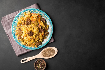 Fragrant pilaf with meat and vegetables top view on a plate on black background with copy space.