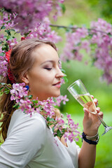 Beautiful woman with a glass of champagne in a cherry blossom garden