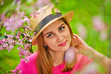 Portrait of a young woman in a hat in a spring park near a blooming pink apple tree. Spring time
