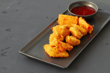 Deep fried chicken nuggets served with chili sauce on gray background