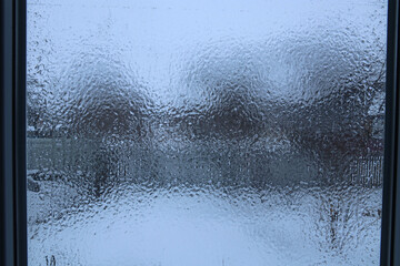 View through a window covered with a layer of ice. Raindrops frozen on the window pane.