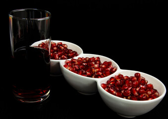 juicy red pomegranate seeds in white bowls and a glass of juice