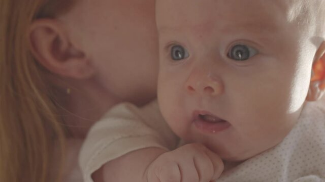 Close up shot of lovely 3 month old baby girl looking at something with interest while being on mother arms