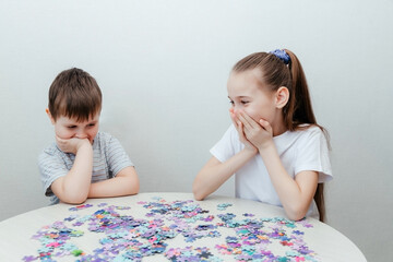 Happy boy and a girl collect a puzzle sitting at a table