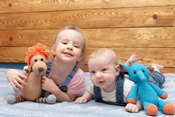 two smiling little children (brother and sister) with toys in denim suits lie on the bed 