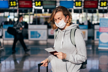 A young woman in a medical protective mask stands at the airport and waits for check-in.