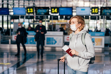 A young woman in a medical protective mask stands at the airport and waits for check-in.