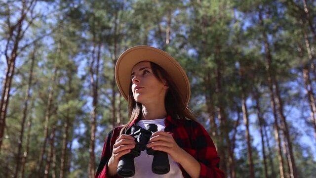 Woman in a hat holds binoculars while hiking in forest. Concept hike, tourism