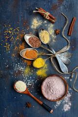 Bright aromatic spices and seeds for baking and cooking on spoons on a dark background, top view.