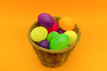 Wicker basket with colorful Easter eggs on yellow background.
