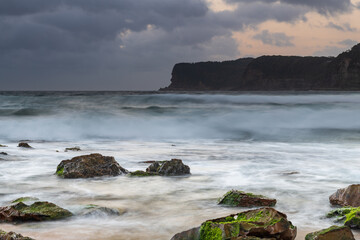 Grey clouds and rocky foreground overcast sunrise at the beach