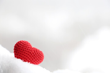 Love heart in the snow, background for Valentine's day card with blurred copy space. Red knitted symbol of romantic love