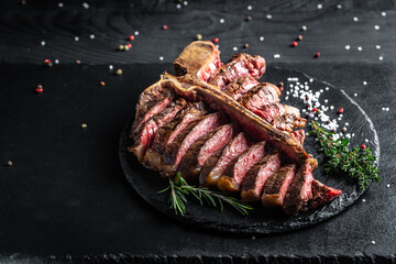 Beef T-Bone steak or aged wagyu porterhouse grilled beef steak Medium rare on a black table....