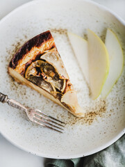 Flat-lay of vegan dairy-free sugar-free pear cheesecake piece and slices of fresh pear in rustic plate over white marble table background, top view. Modern vegetarian healthy dessert concept