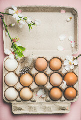 Easter holiday background. Flat-lay of natural colored eggs in box with almond blossom flower branch and feather, pink background, top view, copy space, vertical composition. Greeting card concept