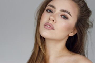 Fototapeta premium The face of a young beautiful girl with natural makeup, beauty portrait. Clear skin and an expressive look on the girl's face, on a gray background.