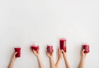 Human hands holding glasses and jar with purple beet pomegranate fresh smoothie with glass straws over white wall background, copy space. Detox, dieting, weight loss, healthy lifestyle concept