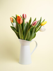 Bouquet of fresh tulip flowers in metal vase on pastel beige background. Minimal spring bloom concept.