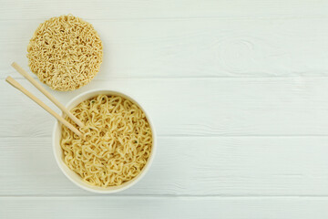 Paper bowl with noodles and chopsticks on white wooden background