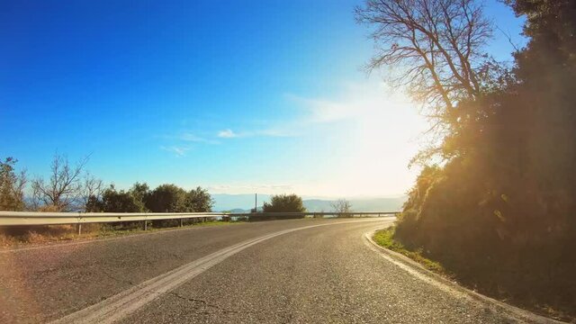 POV driving along mediterranean coast, curvy asphalt road, landslide barrier, shining sun clear blue sky horizon, car travel gopro point of view