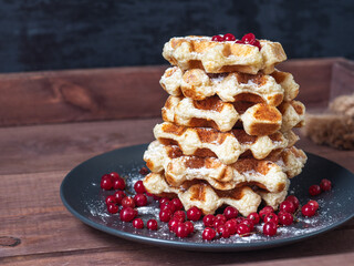 Fresh-baked Viennese waffles with powdered sugar and berries on a black plate