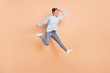 Fototapeta na wymiar Full size profile photo of optimistic nice brunette lady jump look wear blue sweater jeans sneakers isolated on beige background