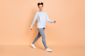 Fototapeta na wymiar Full size profile photo of optimistic nice brunette lady go wear light blue sweater jeans sneakers isolated on pastel beige color background