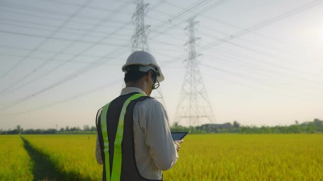 Electrical engineer worker in helmet  working near tower with electricity. business energy technology industry concept. electrician studying reading documents on a tablet
