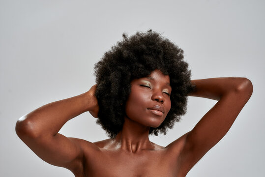 Portrait of sensual african american female model with afro hair and perfect glowing skin posing with eyes closed isolated over gray background