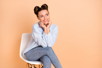 Photo of optimistic cool brunette lady sit look empty space hands fists wear sweater jeans isolated on pastel beige color background