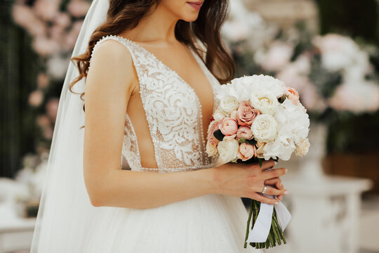 Tender bride holds a bouquet with white and pink roses in her hands. Close-up and cropped shot.