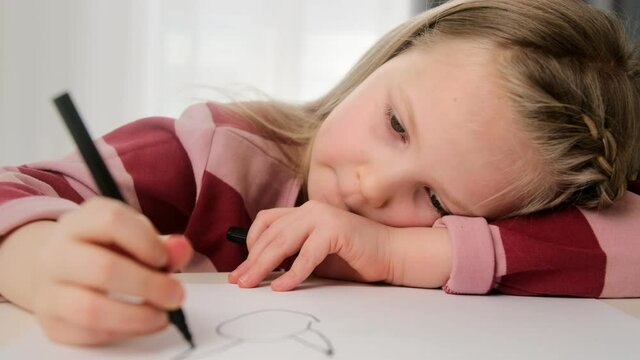 Sad child a little girl is bored and draws a picture with her head down. Depression and relationship problems are tested by a psychologist.