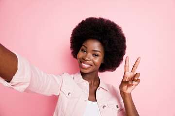 Self-portrait of cute lovely cheerful wavy-haired girl showing v-sign isolated over pink pastel color background