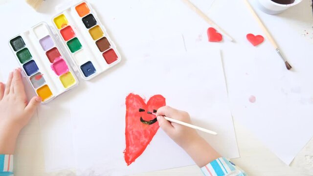 little girl draws funny hearts with watercolors, Kids art. Crafts concept. How to make a greeting card, Creating handmade gifts for Mothers Day or kids birthday