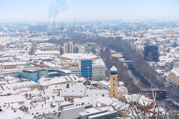 Fototapeta na wymiar Cityscape of Graz with the Franciscan Church tower and historic and modern buildings of Graz, Styria region, Austria, with snow, in winter