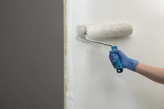 Hand Using Masking Tape And A Roller To Paint Gray Wall White