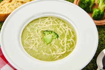 Healthy broccoli cream soup in bowl on green grass background. Diet detox food concept
