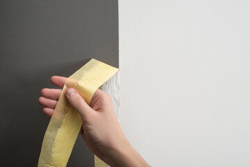 Hand taking off masking tape from the wall