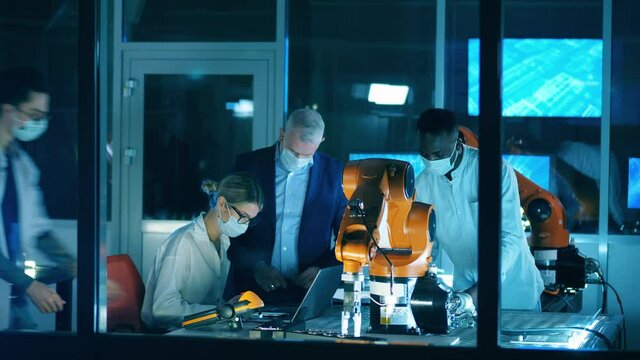 Scientists in face masks are observing robots in the lab