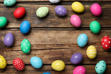 Frame of colorful eggs on wooden background, flat lay with space for text. Happy Easter