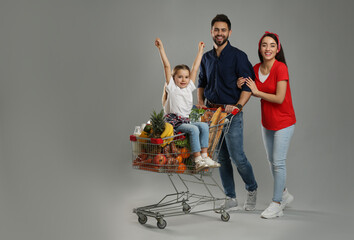 Happy family with shopping cart full of groceries on grey background